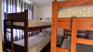 Habitació amb dos llits superposats, una finestra amb cortines i un terra de fusta.