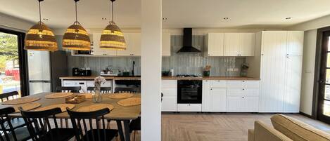 A modern kitchen with white cabinets, a dining area with a wooden table and black chairs, and pendant lighting.