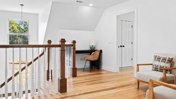 Habitación amplia con escalera de madera, un escritorio y una silla, y una puerta que da a otra habitación.