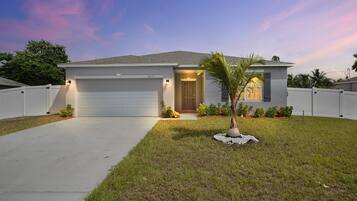 A single-story house with a garage, a front door, and a small lawn with a palm tree.