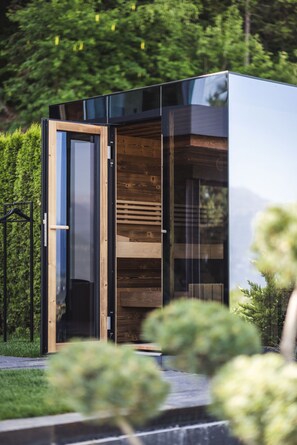 A modern, compact building with a glass door entrance, wooden interior, and a view of a lush green landscape.