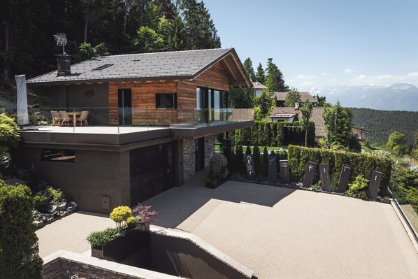 A modern house with a glass balcony, a stone facade, and a view of a mountainous landscape.