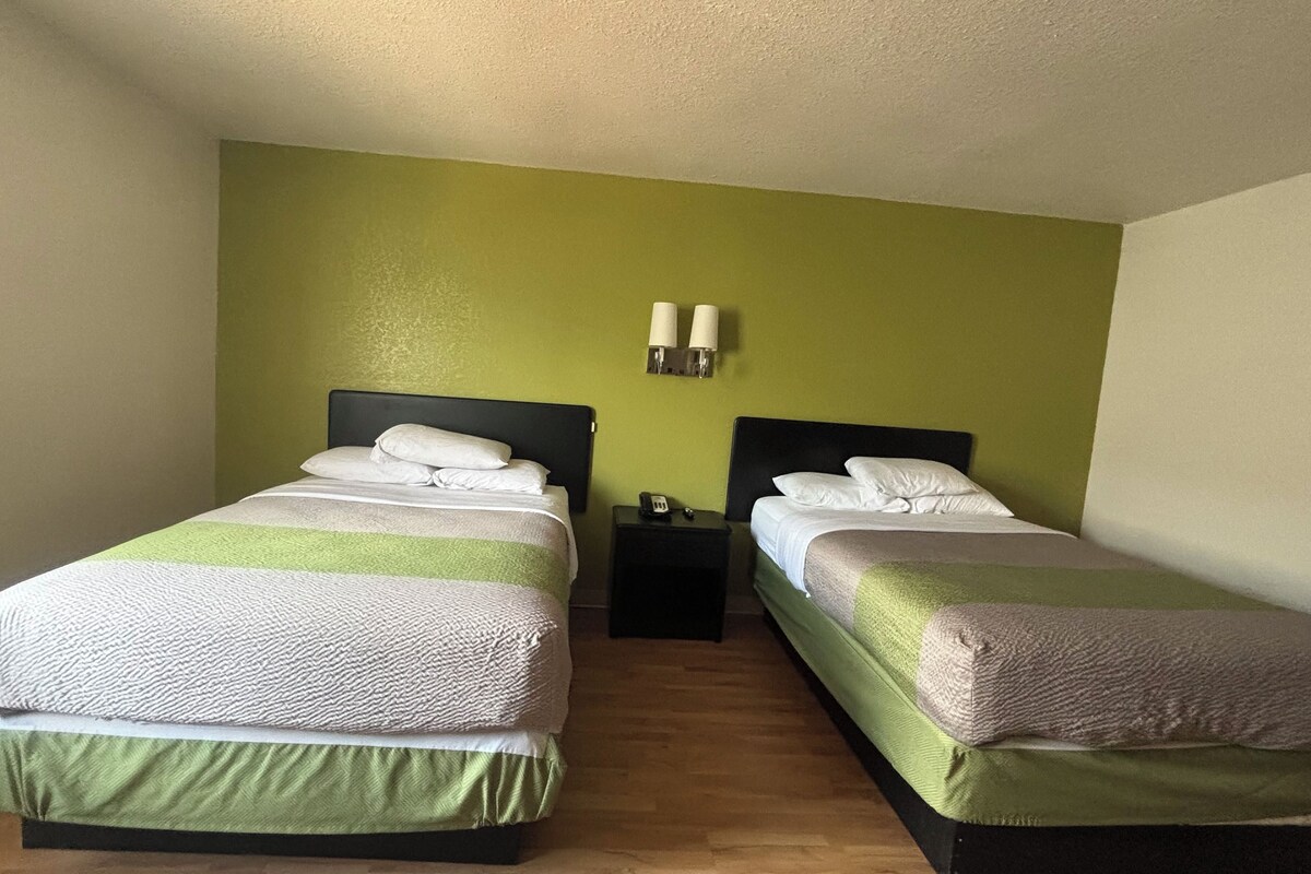 A twin room with two beds, a nightstand, and a wall-mounted lamp.