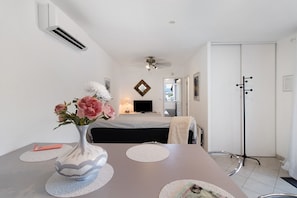 A hotel room with a bed, a desk with a vase of flowers, a television, and a coat rack. - Villa “Pavillon 1013” with Private Pool, Terrace & Wi-Fi (Bastelicaccia)
