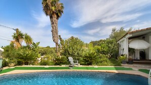 A swimming pool with a surrounding garden, a tall palm tree, and a building with a covered porch.