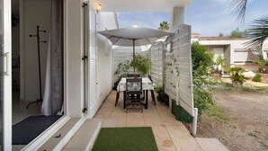 A patio with a table and chairs, a white umbrella, and a small garden area.