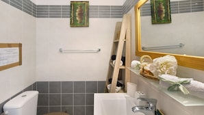 A bathroom with a toilet, sink, and mirror. There is a towel rack and a wooden ladder leaning against the wall.