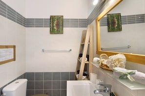 Une salle de bain avec des toilettes, un lavabo et un miroir. On y trouve un porte-serviettes et une échelle en bois appuyée contre le mur.
