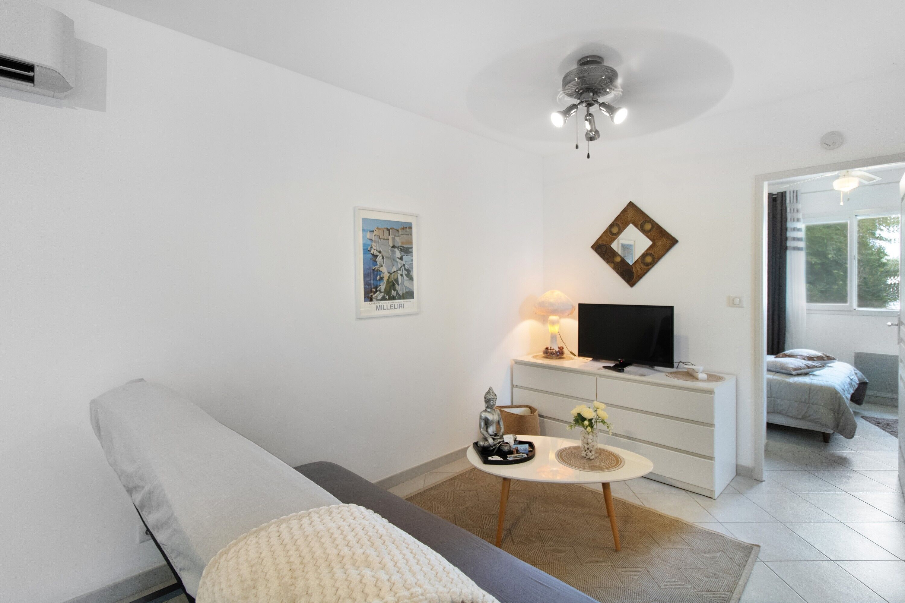 Un salon moderne avec un canapé gris, une petite table ronde sur laquelle est posée une statue de Bouddha, un téléviseur à écran plat et un tableau accroché au mur.