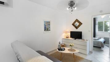 Un salon moderne avec un canapé gris, une petite table ronde sur laquelle est posée une statue de Bouddha, un téléviseur à écran plat et un tableau accroché au mur.