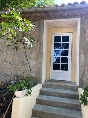 Una serie di gradini in cemento che conducono a una porta bianca con una finestra, circondata da un muro in pietra e vegetazione.