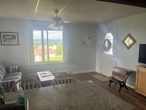 Ein Wohnzimmer mit Essbereich, Deckenventilator, Blick durch ein Fenster und einer Tür mit einem Kranz.