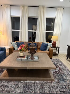 Ein Wohnzimmer mit einem braunen Ledersofa, einem Couchtisch mit einer Zierurne und einem gemusterten Teppich.
