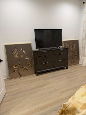 Ein Schlafzimmer mit einem dunklen Holzschrank, einem Flachbildfernseher und zwei dekorativen Wandpaneelen mit floralen Mustern.