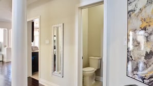Um corredor com espelho, porta de acesso a um banheiro e quadro na parede.
