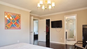 Quarto com cama, televisão, lustre e uma obra de arte colorida na parede.