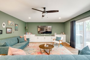 Ein Wohnzimmer mit Deckenventilator, Flachbildfernseher, Sofa, Couchtisch und einem gemusterten Teppich.