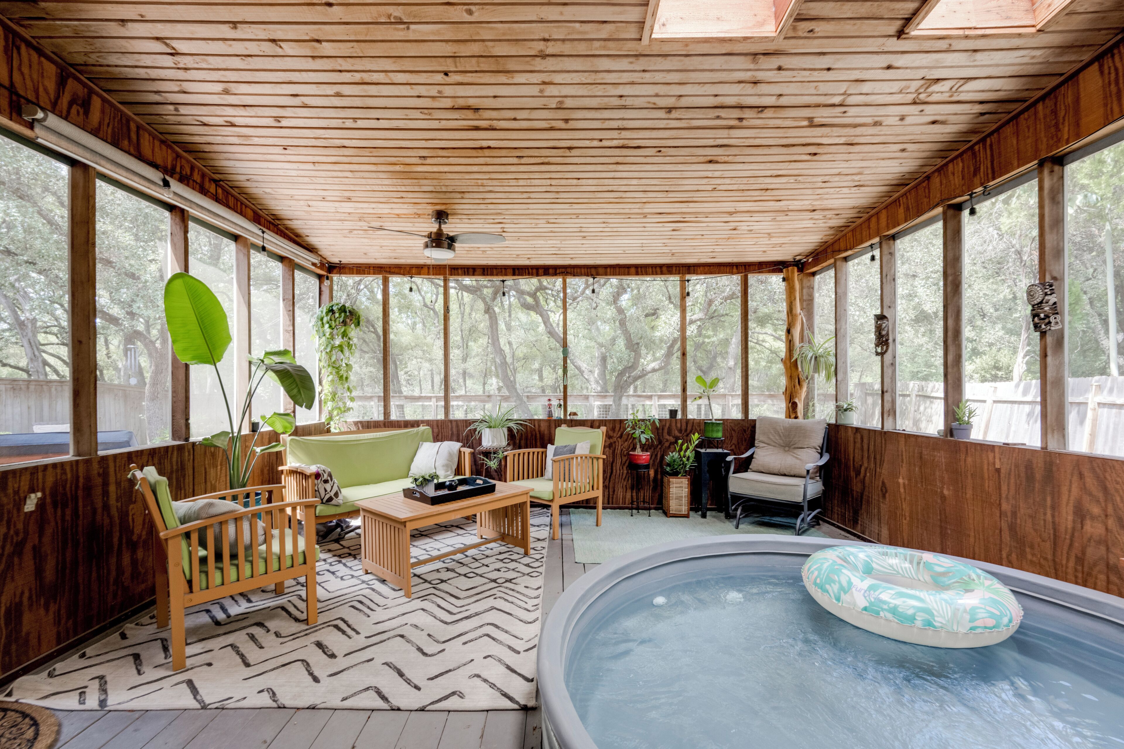 A covered outdoor area with a hot tub, seating, and potted plants.