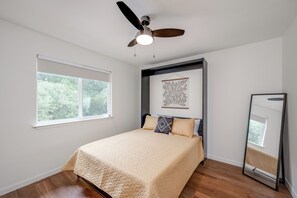 Ein Schlafzimmer mit Bett, Deckenventilator, Fenster und einem Wandbild.