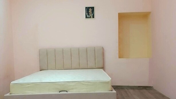 A bedroom with a bed, a small wall-mounted shelf, and a window.