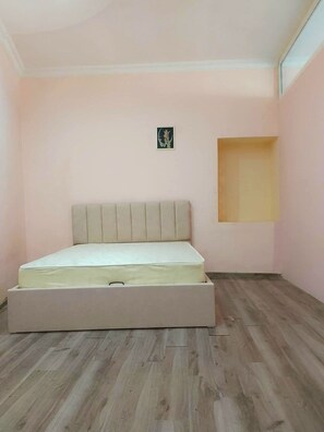A bedroom with a bed, a small wall-mounted shelf, and a window.