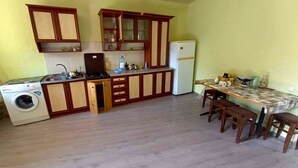 A compact kitchen with wooden cabinets, a built-in washing machine, and a dining area with a table and chairs.