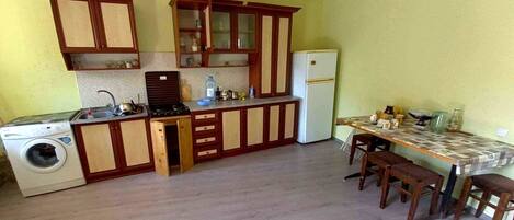 A compact kitchen with wooden cabinets, a built-in washing machine, and a dining area with a table and chairs.