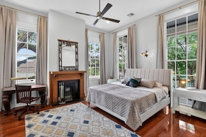 Quarto com cama, escrivaninha, lareira e grandes janelas.