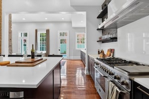 Cozinha moderna com uma ilha grande, eletrodomésticos de aço inoxidável e vista para o exterior.