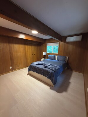 A bedroom with a bed, wooden walls, a window, and an air conditioning unit. - Casita del Mar near Sandlake and Buzzard Butte Trail Network. 4 bedrooms (Cloverdale)