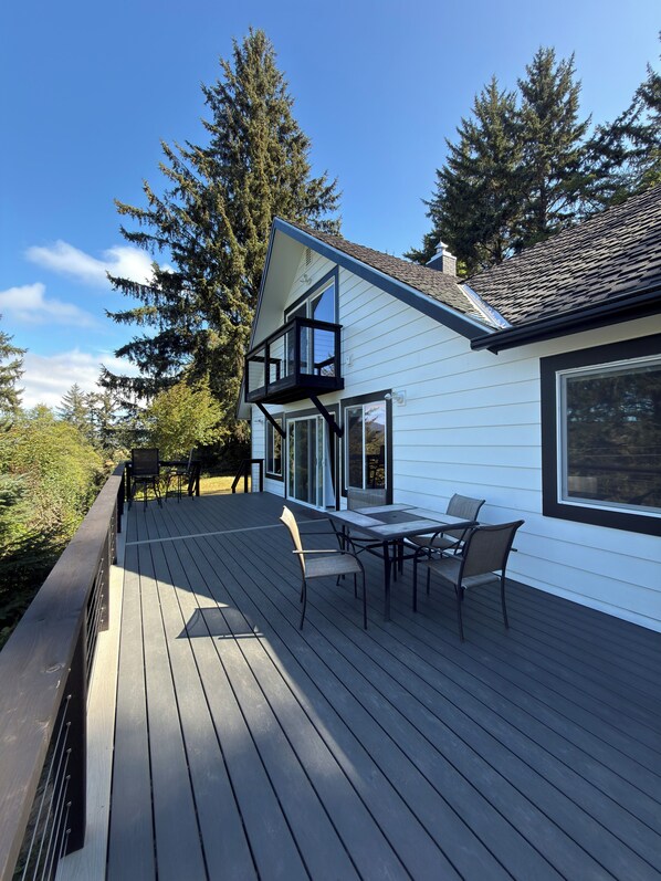 A deck with outdoor furniture, a glass balustrade, and a house with white siding and a dark roof. - Casita del Mar near Sandlake and Buzzard Butte Trail Network. 4 bedrooms (Cloverdale)