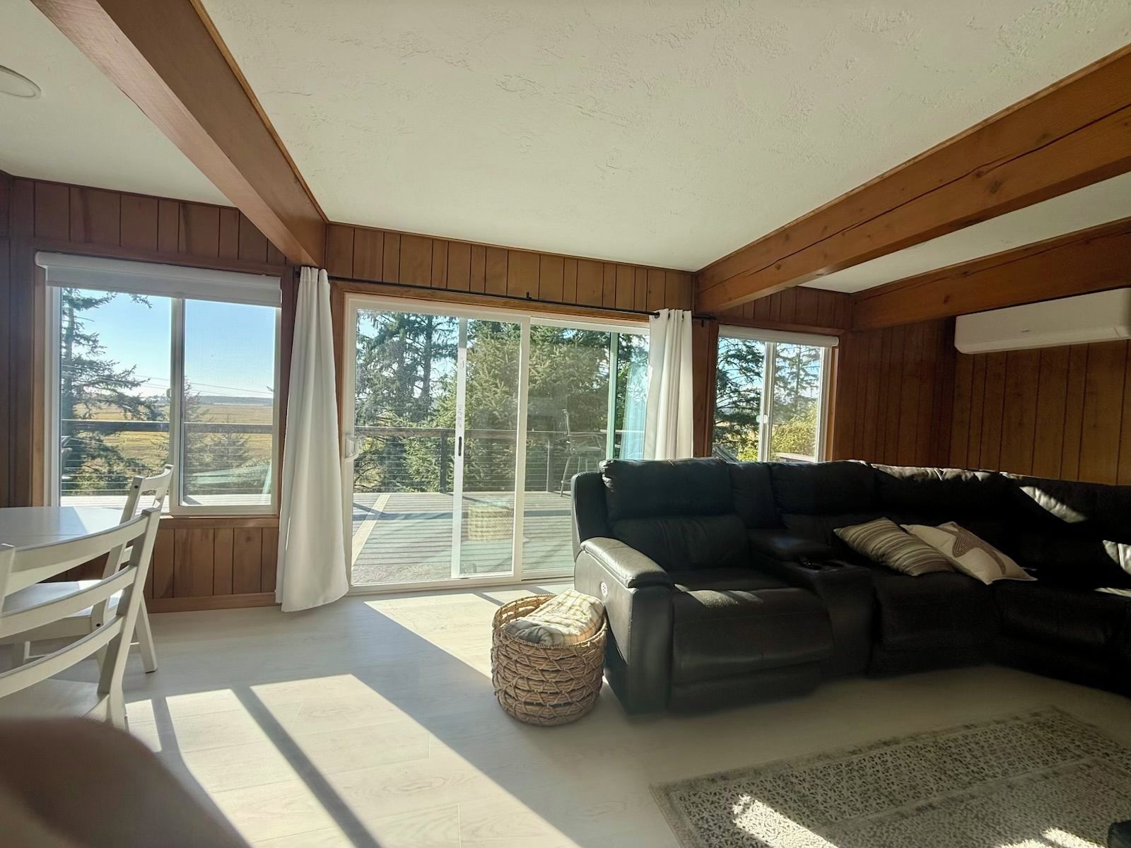 A living room with a black leather sofa, a white dining table, and a view through large sliding glass doors to an outdoor deck.