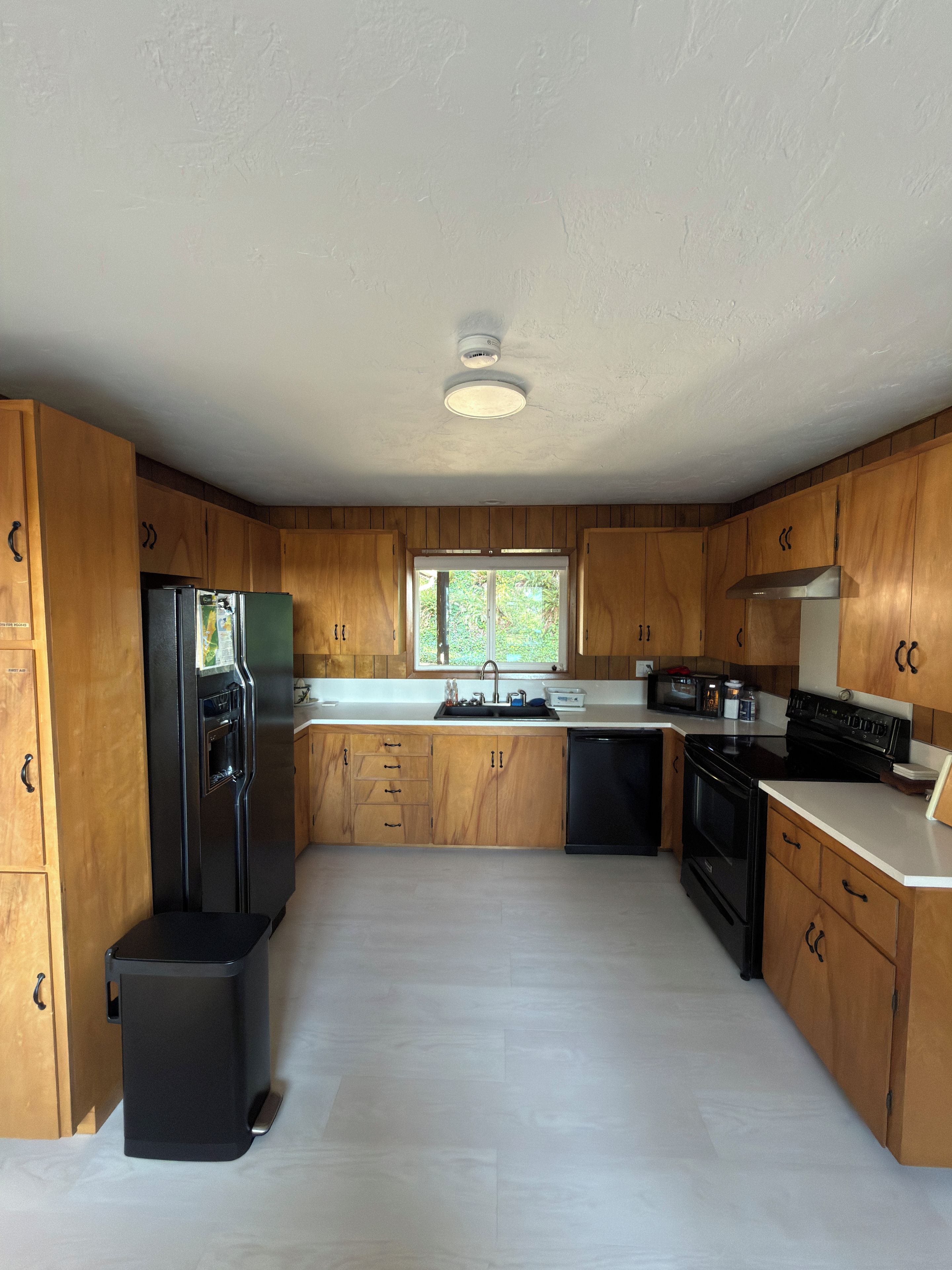 Una cocina con gabinetes de madera, un refrigerador negro, un lavamanos y una estufa.