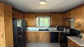 Una cocina con gabinetes de madera, un refrigerador negro, un lavamanos y una estufa.