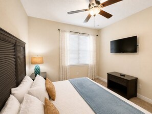 A hotel room with a bed, a ceiling fan, a TV, and a window with curtains. - Reunion Resort 6BR Pool Home & Game Room (Kissimmee)