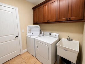A laundry area with a washer and dryer, a sink, and wooden cabinets. - Reunion Resort 6BR Pool Home & Game Room (Kissimmee)