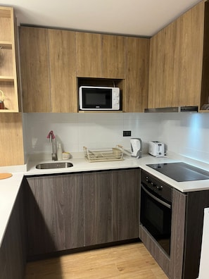 Une cuisine compacte avec des meubles en bois, un four à micro-ondes, un évier, un grille-pain et une cuisinière.