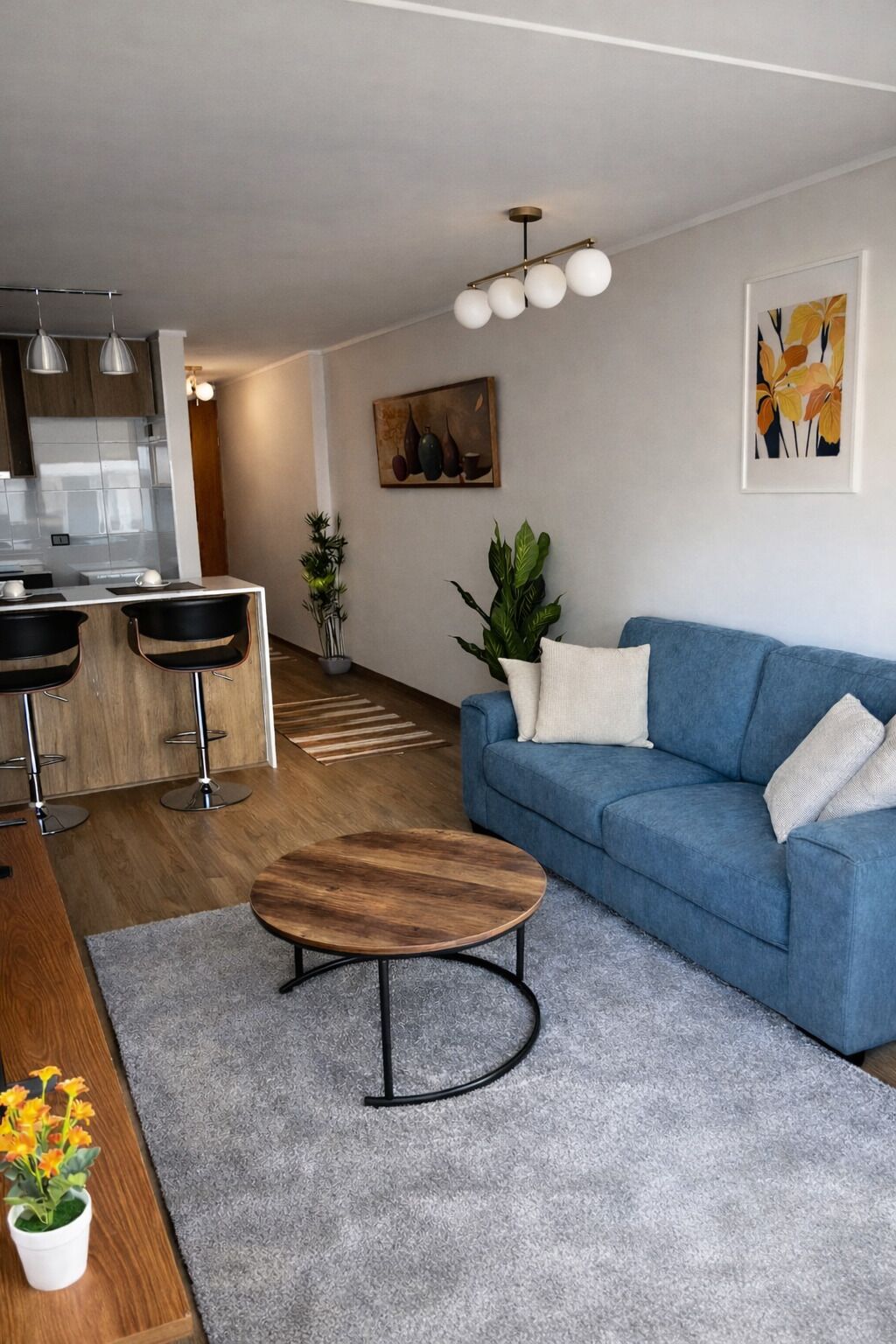 Un salon moderne avec un canapé bleu, une table basse en bois et un coin cuisine doté de tabourets de bar.