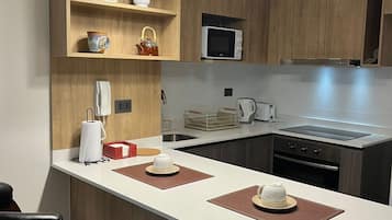 A modern kitchen with wooden cabinets, a white countertop, a microwave, a kettle, and pendant lights.