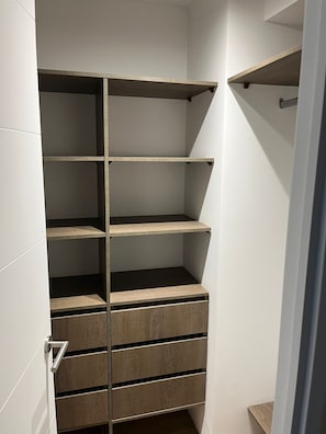 A walk-in closet with multiple shelves and drawers, a door with a handle, and a light switch on the wall.