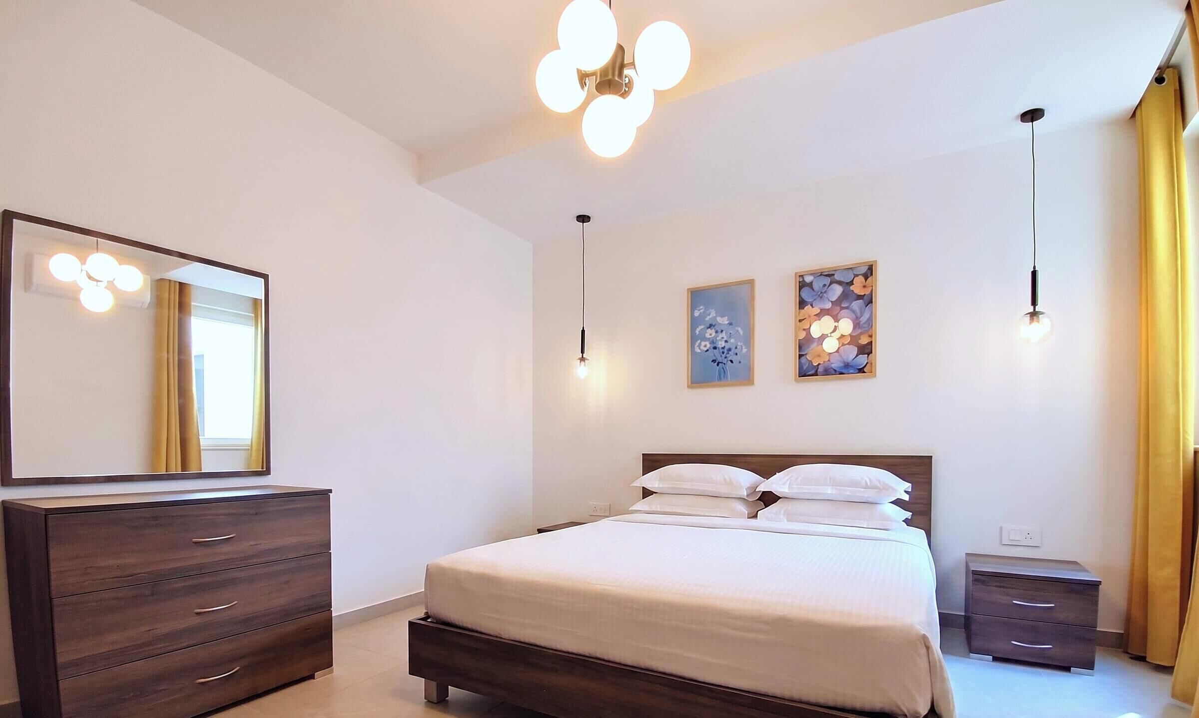 Un dormitorio con una cama, un aparador, un espejo y dos lámparas de pared.