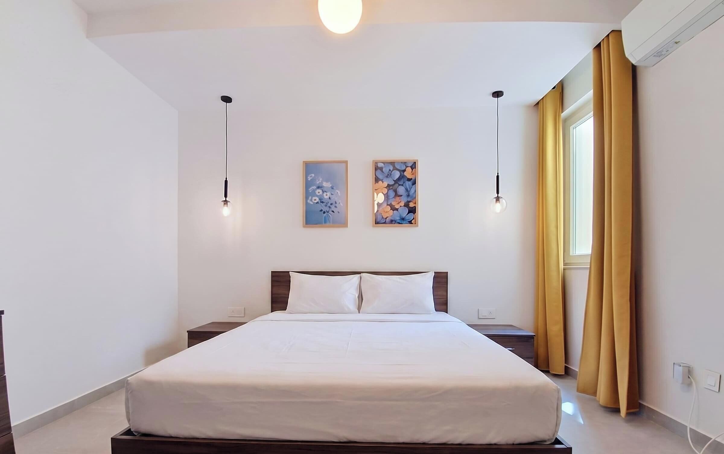 Une chambre d’hôtel avec un grand lit, deux appliques murales et deux tableaux représentant des motifs floraux, encadrés.