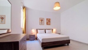A modern bedroom with a wooden bed, bedside tables, a mirror, and two wall-mounted paintings. - Gozo Stay: 2BR Apt with Balcony in Xagħra Village (Ix-Xagħra)