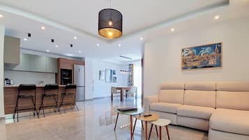 Una sala moderna con un sofá, un comedor con sillas, una cocina con taburetes de bar y una lámpara colgante.