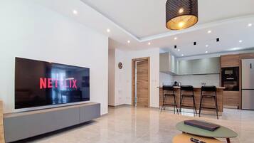 Una sala de estar moderna con un televisor de pantalla plana, una mesa de centro y una zona de cocina con taburetes de bar.