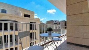 A balcony with a round table and chairs, a potted plant, and a view of adjacent buildings. - Gozo Stay: 2BR Apt with Balcony in Xagħra Village (Ix-Xagħra)