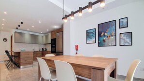 A modern kitchen with a wooden island, a dining area with a wooden table and white chairs, and a wall with framed artwork. - Gozo Stay: 2BR Apt with Balcony in Xagħra Village (Ix-Xagħra)