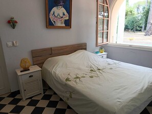 A bedroom with a checkered floor, a bed with a floral bedspread, a nightstand with a lamp, and a painting on the wall. - Villa with pool & view of the Gulf of Saint-Tropez (Saint-Tropez)