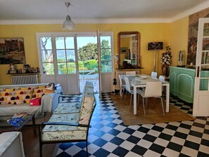 Ein Essbereich mit Schachbrettmuster-Boden, einem Esstisch, Stühlen und Blick durch ein großes Fenster.