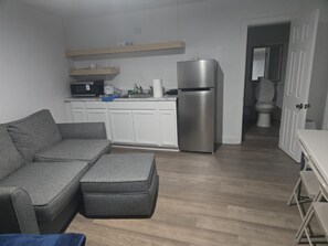 A compact kitchen with white cabinets, a stainless steel refrigerator, a microwave, and a sink. - Beautiful 1-bedroom house with AC in fantastic North Miami (North Miami)
